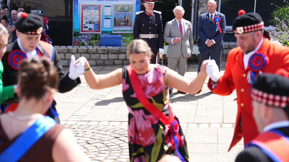 A group of dancers performing on a street while the King watches on in the background