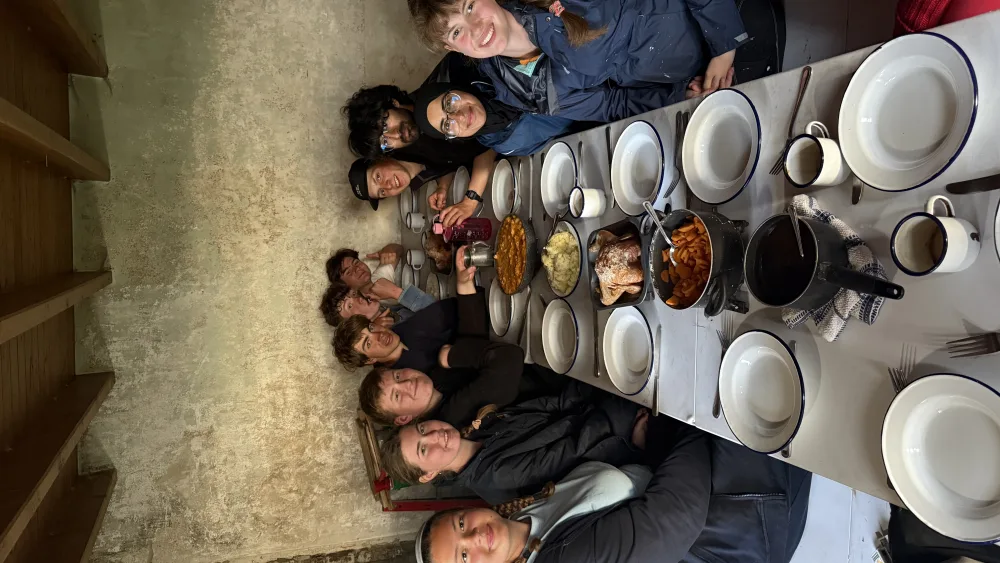 A group of teenagers smiling while seated around a dinner table