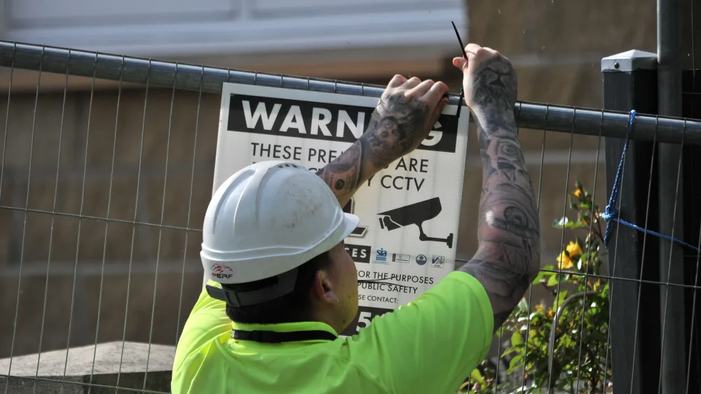 A worker in hard hat puts up a warning sign on fencing