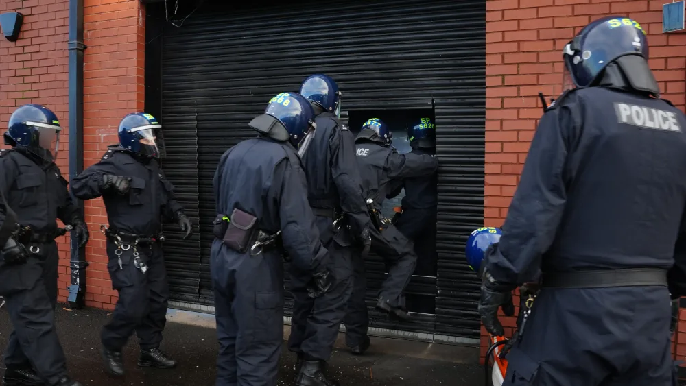 Police officers in protective helmets enter a property through a shutter