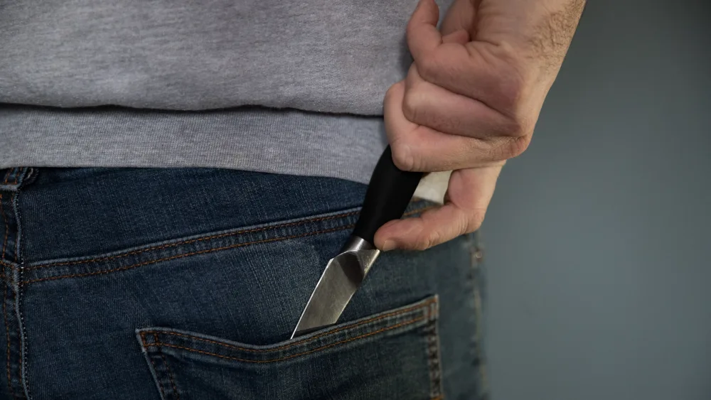 A man holding a knife which is in their back pocket