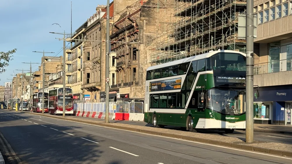 Buses travelling along Princes Street, with a fire-damaged building in the background
