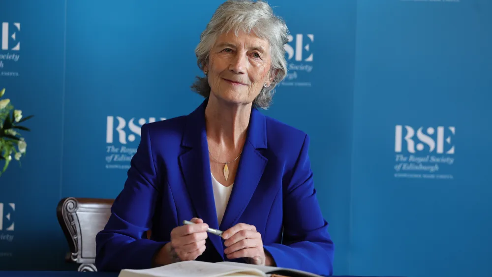 Catherine Connolly smiling while seated, holding a pen in front of RSE signage