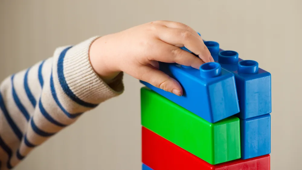 The arm of a child playing with colourful building blocks