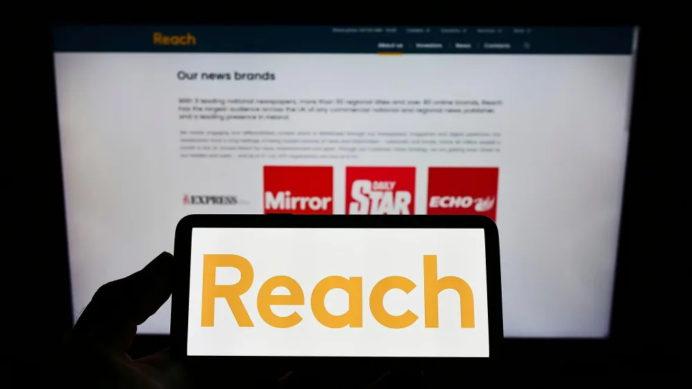 The Reach logo displayed on a smartphone in front of the business webpage