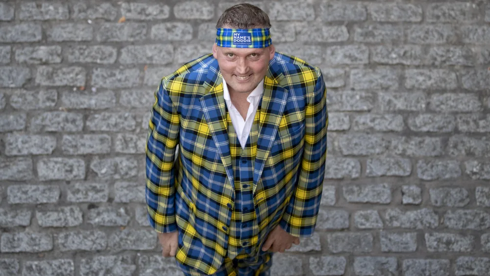 Doddie Weir smiling, while wearing a yellow and blue tartan suit and matching bandana