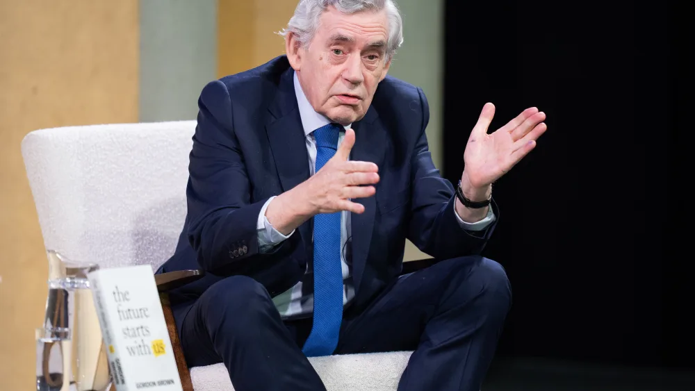 Gordon Brown gesturing with his hands while seated on a stage