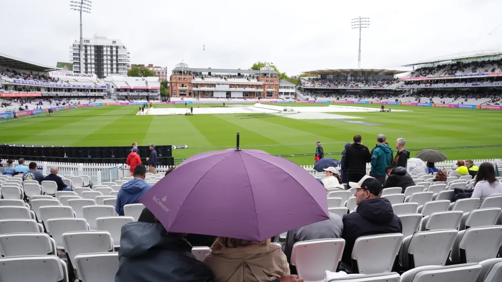 Covers are on as people shelter under a umbrella from rain on day three of the second Rothesay Test match at Lord’s in London