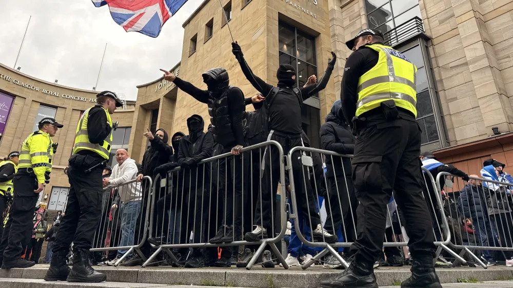 Protesters dressed in black with their arms in the air, while police look on