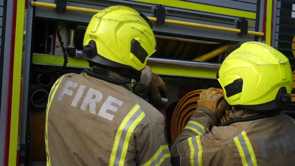 two firefighters viewed from behind, next to a fire engine