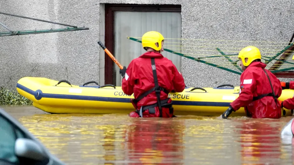 Two men in rescue gear negotiate flood water with a yellow boat