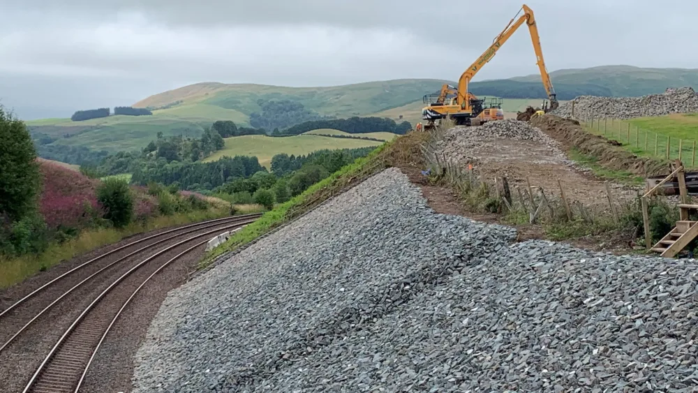 Digger at the top of embankment beside railway