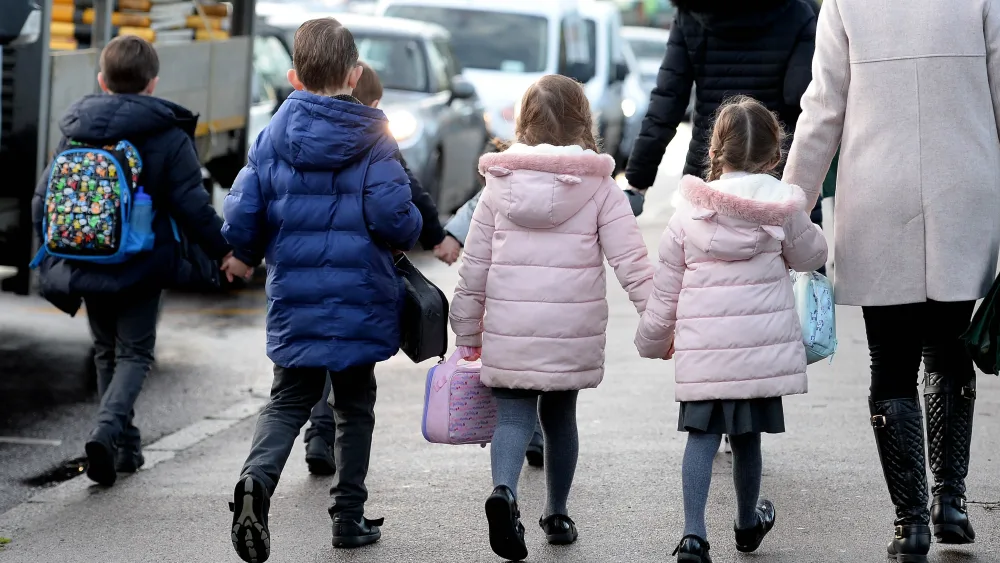 The backs of a group of school children walking along a road