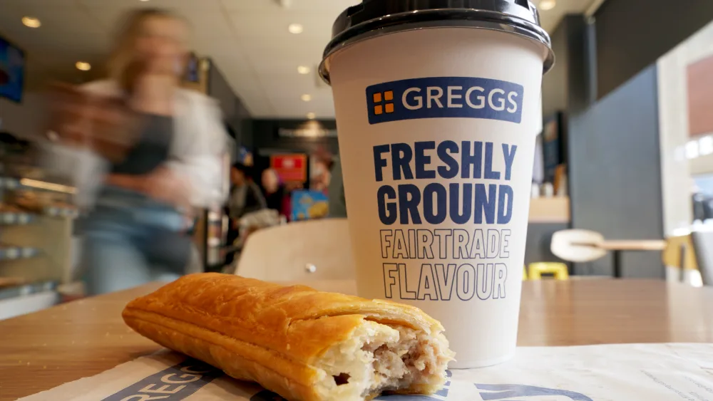 A sausage roll and a coffee sits on a table in a Greggs store