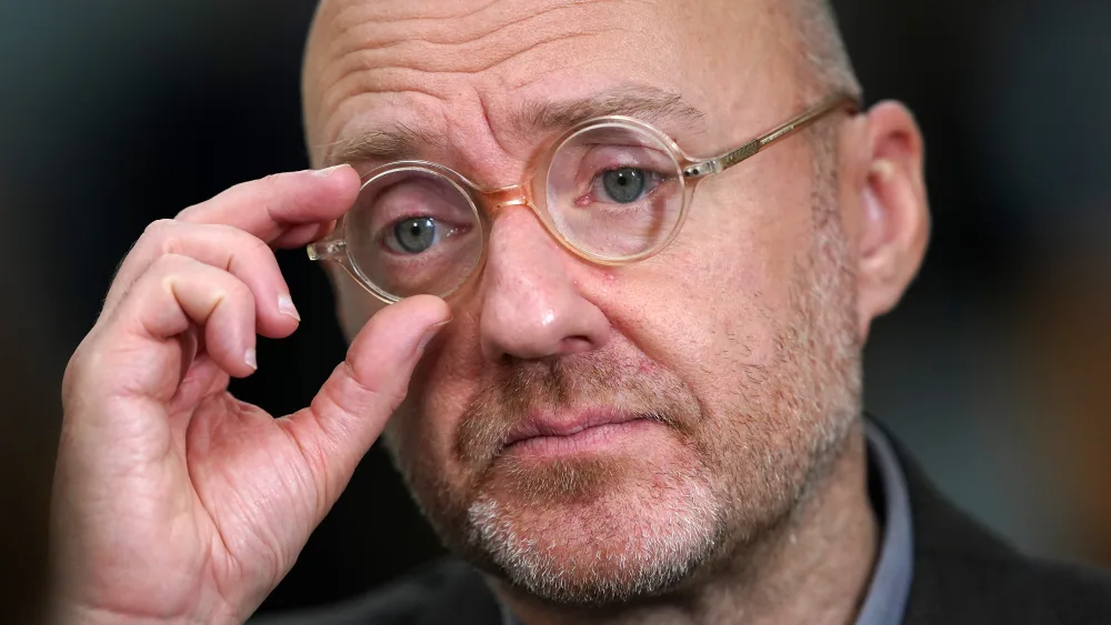 Headshot of Patrick Harvie, adjusting his round glasses