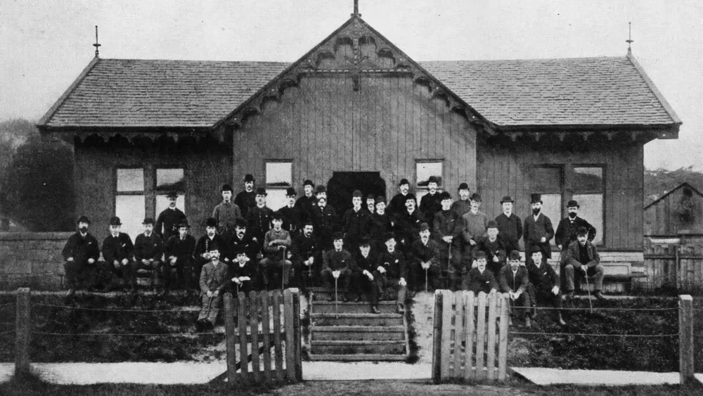 Black and white photo of a group of men standing in front of a football pavilion