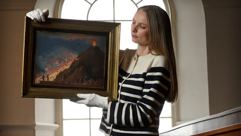 A woman holding a framed painting of Vesuvius erupting