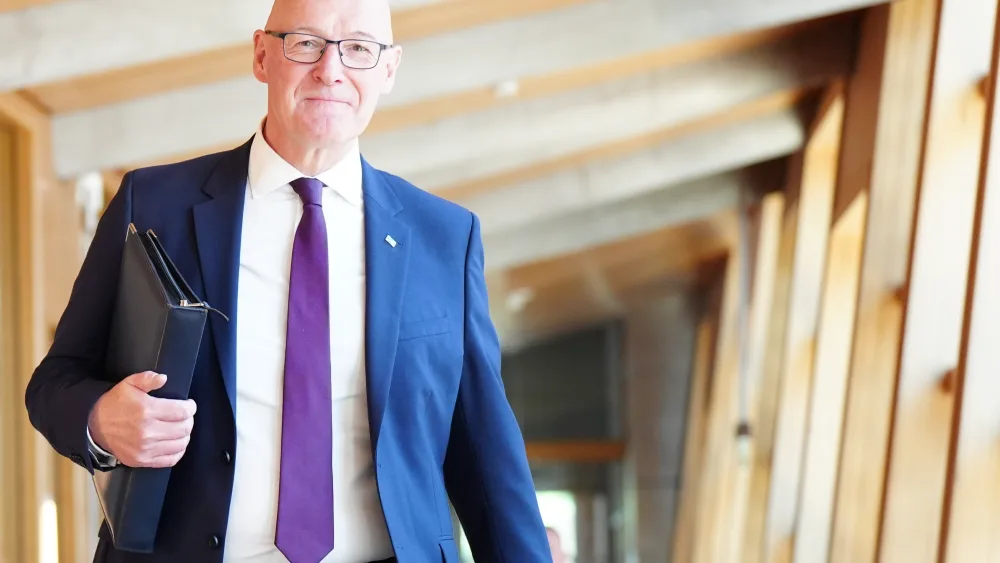 John Swinney holding a folder under his arm while walking inside the Scottish Parliament