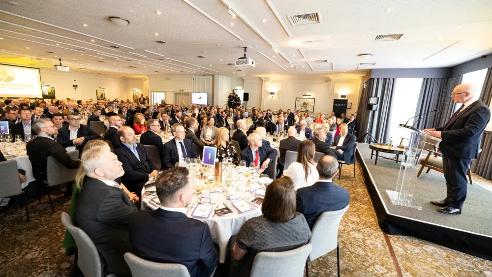 John Swinney speaking from a lectern in a large room filled with tables of people