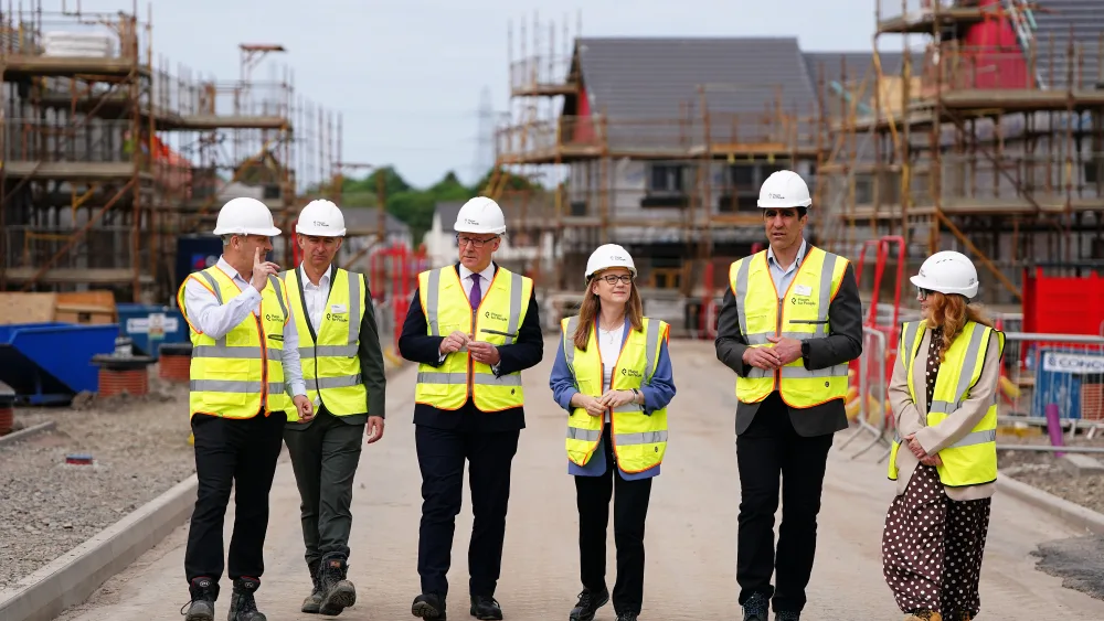 John Swinney and Shirley-Anne Somerville, wearing hi-vis vests and hard hats, walking in a group on a new housing development