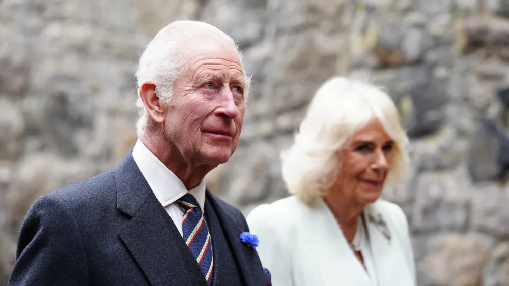 Charles and Camilla walking outside, with a wall behind them