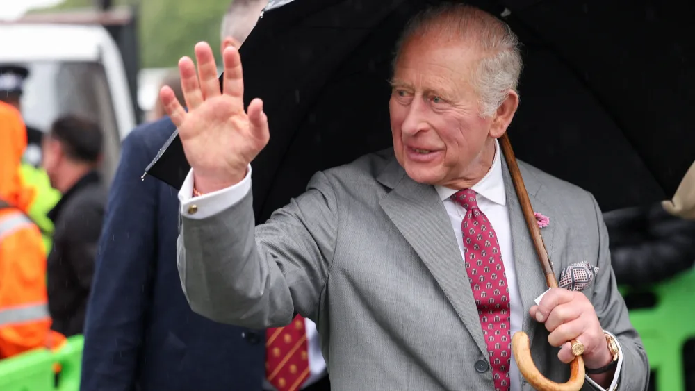 The King, holding a black umbrella, smiles and waves