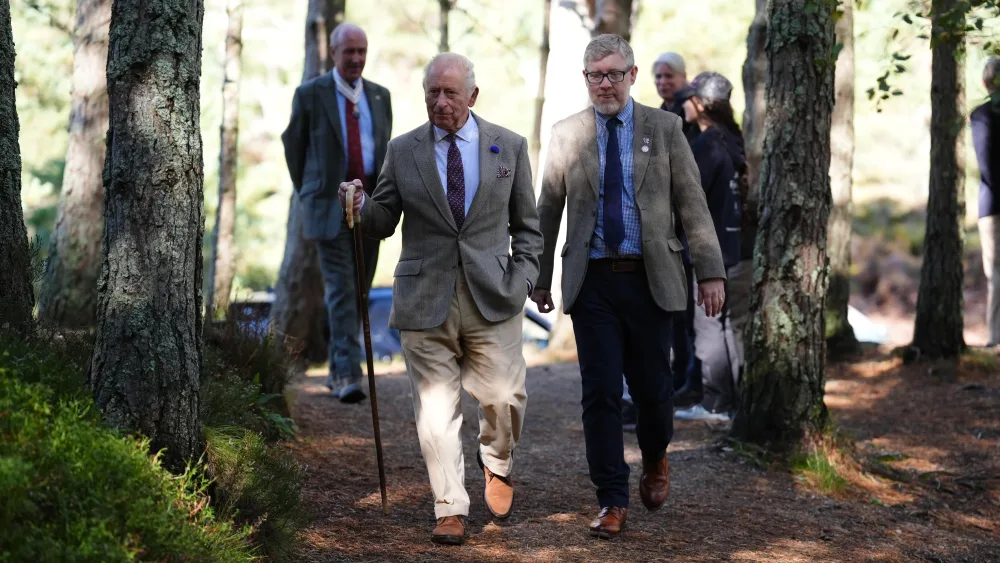 Charles walks through a woodland area, with another man