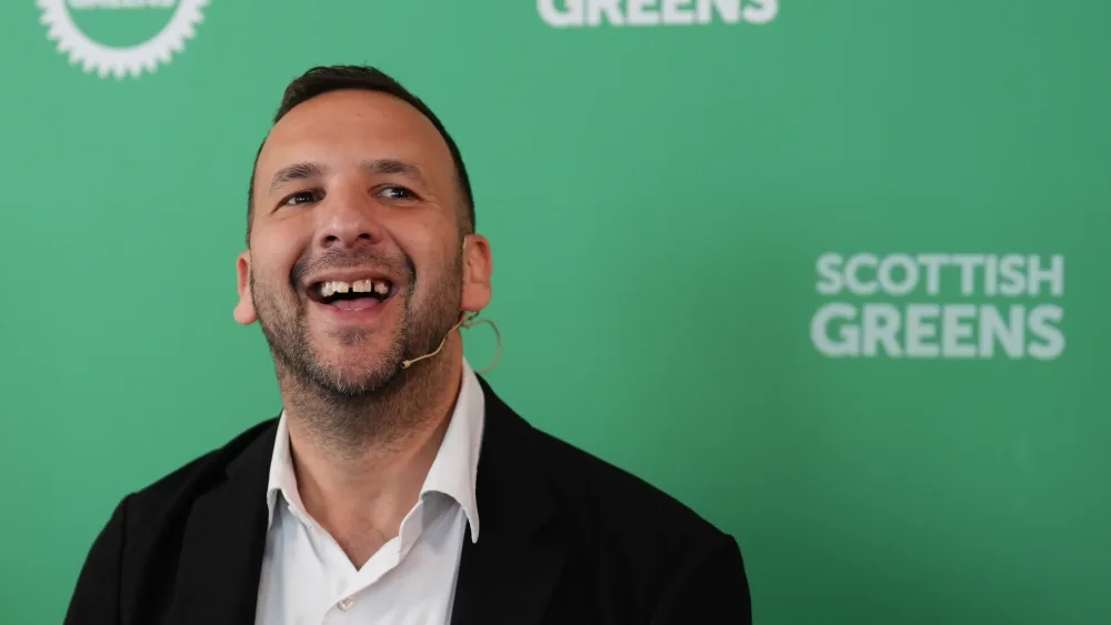 Zack Polanski smiling while speaking in front of Scottish Greens signage