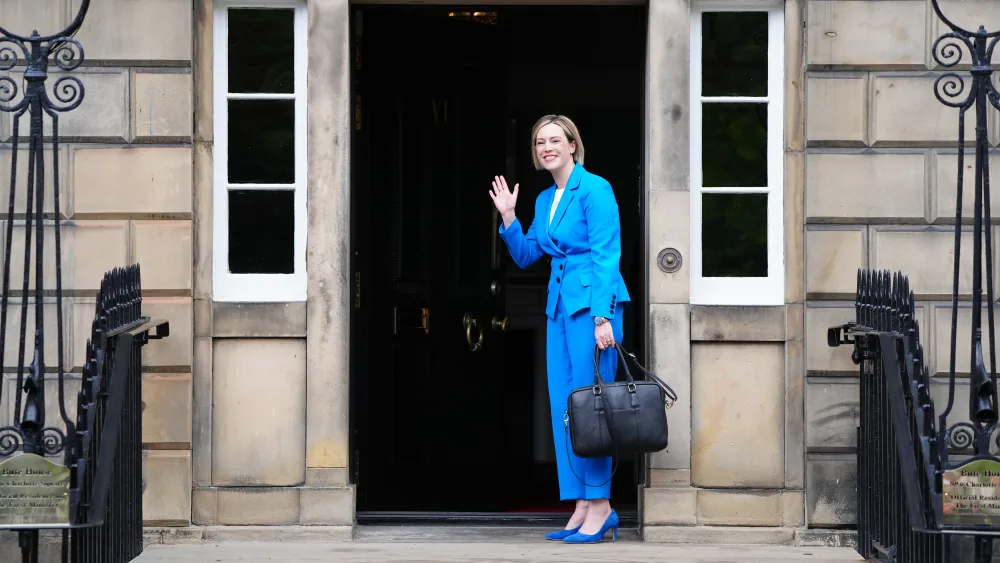 Jenny Gilruth smiling and waving while standing outside Bute House