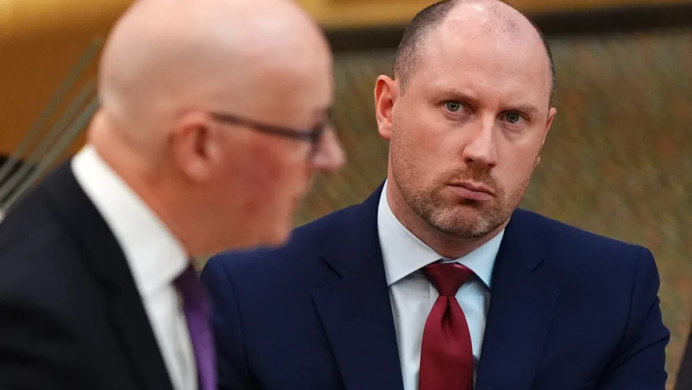 Neil Gray seated in Holyrood, watching on as John Swinney, to his right, is speaking