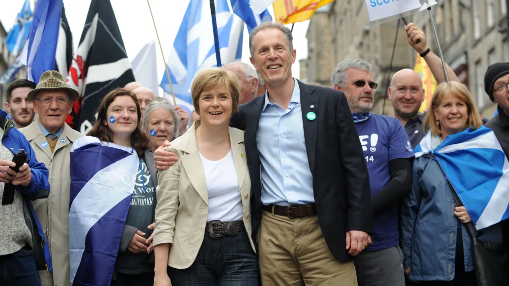 Nicola Sturgeon and Blair Jenkins smiling, while surrounded by people wearing or flying Scottish flags