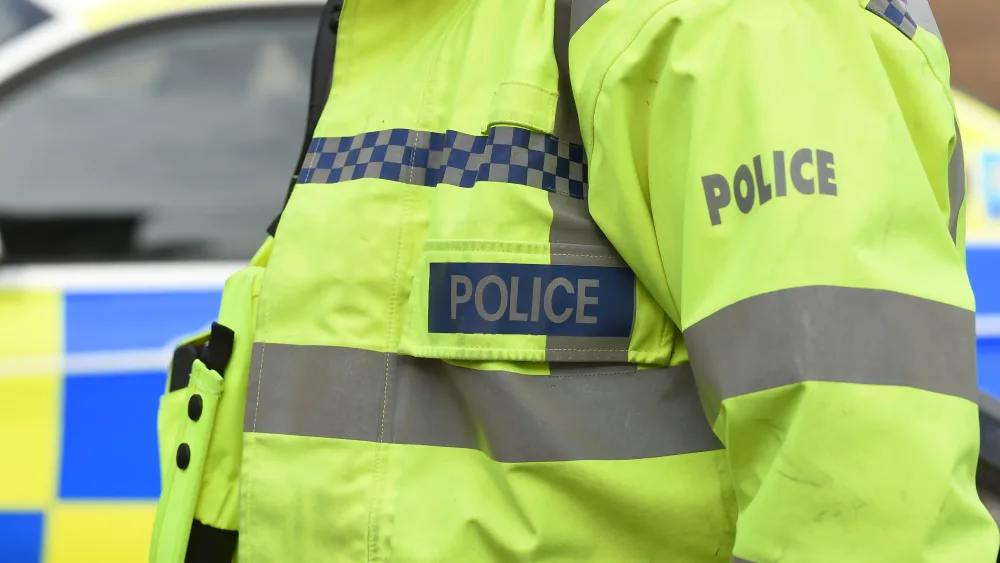 A police officer wearing a hi-vis jacket beside police car