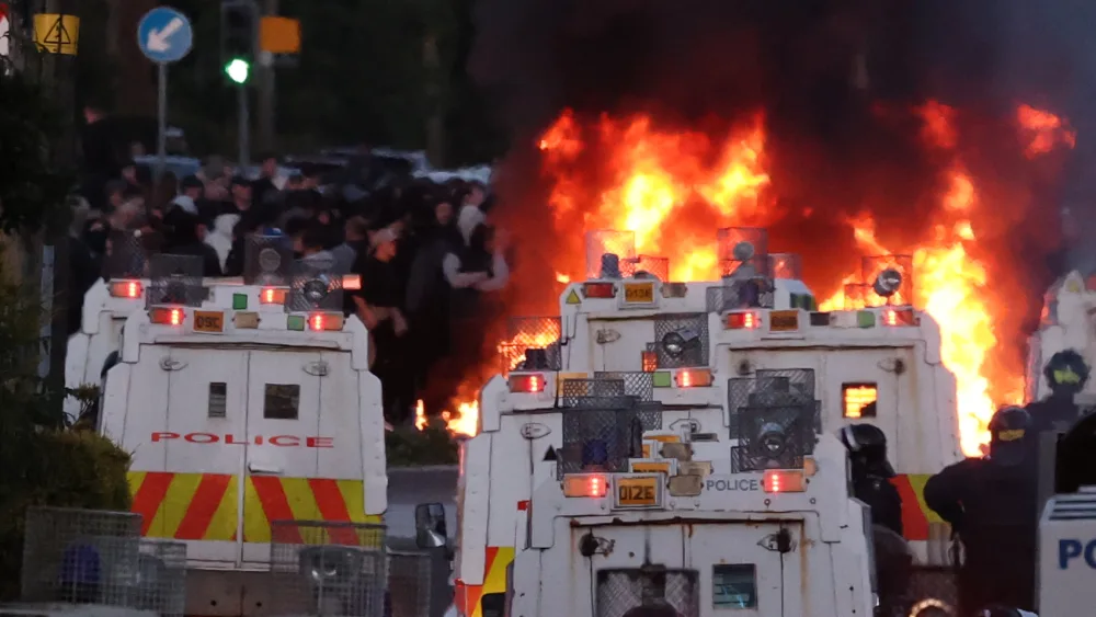 A fire in a street during rioting, with numerous police vehicles and officers in the foreground