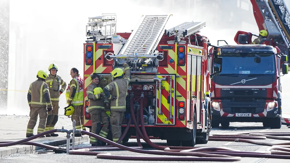 Firefighters and a fire engine at the scene of a blaze, with smoke in the background