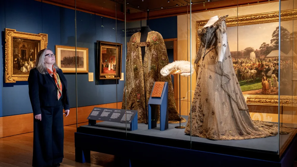 Queen Alexandra's coronation dress in a display cabinet, with a woman looking at it