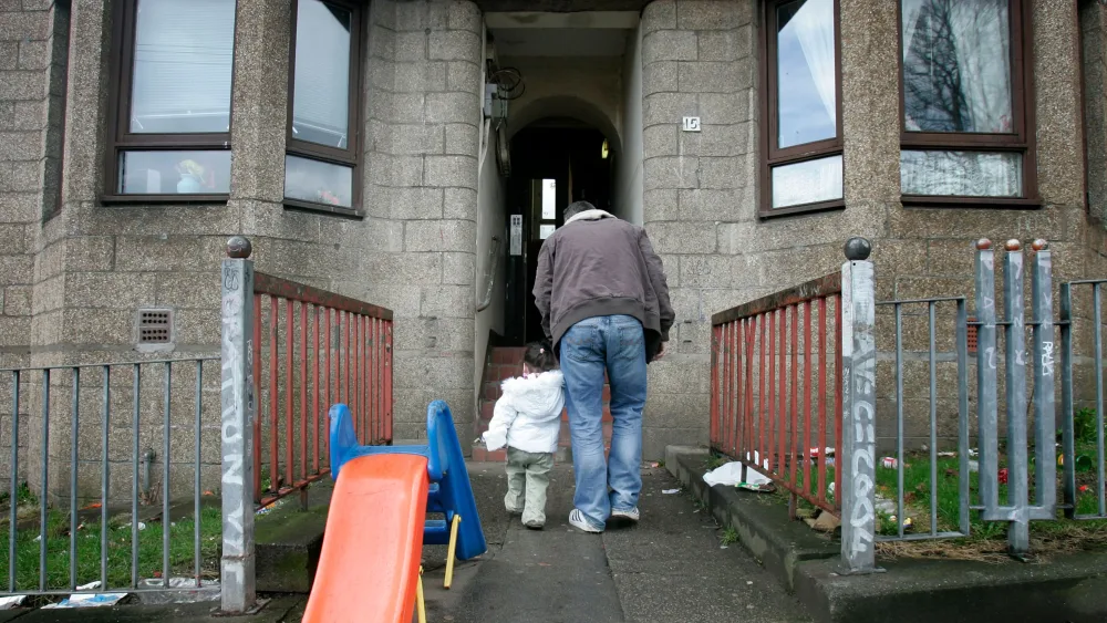 An adult and child enter a rundown block of flats