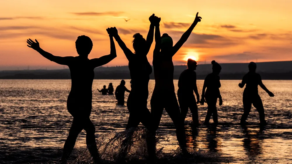 Swimmers with their hands raised, in shallow sea water at sunrise