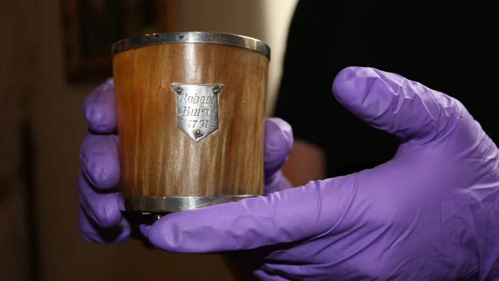 A pair of hands in gloves holding up a cup made of horn