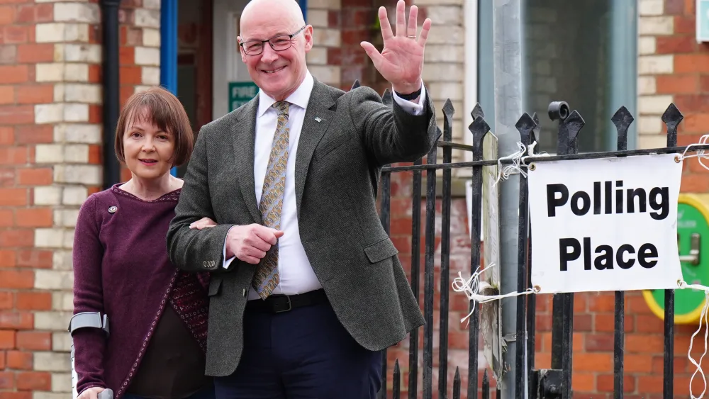 John Swinney waving as he stands with his wife Elizabeth outside a polling station