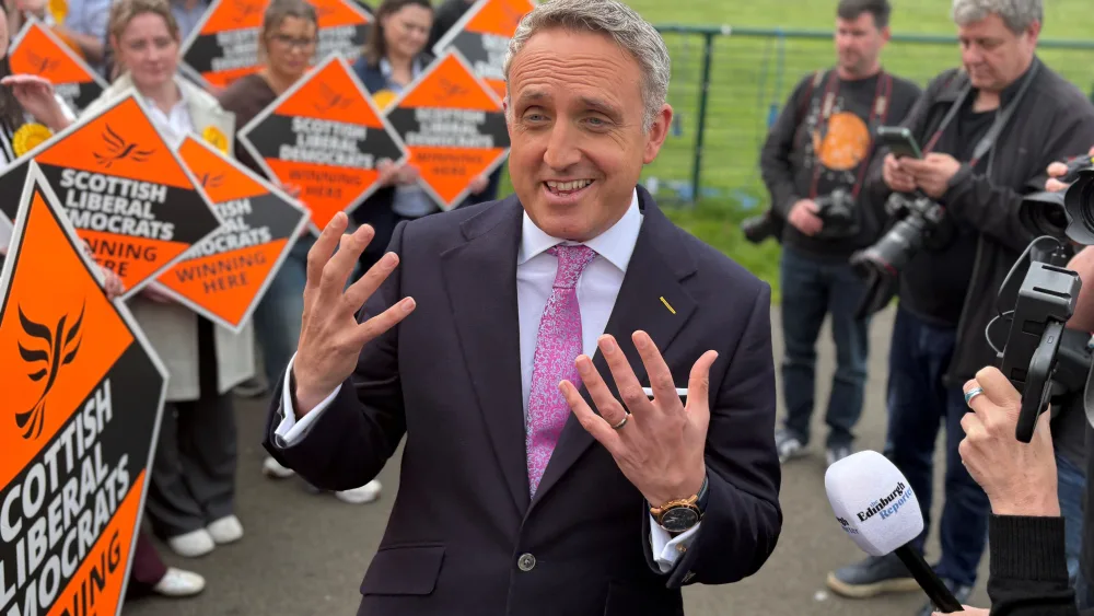 Alex Cole-Hamilton smiling while speaking outside, with a large group of Lib Dem supporters to his right