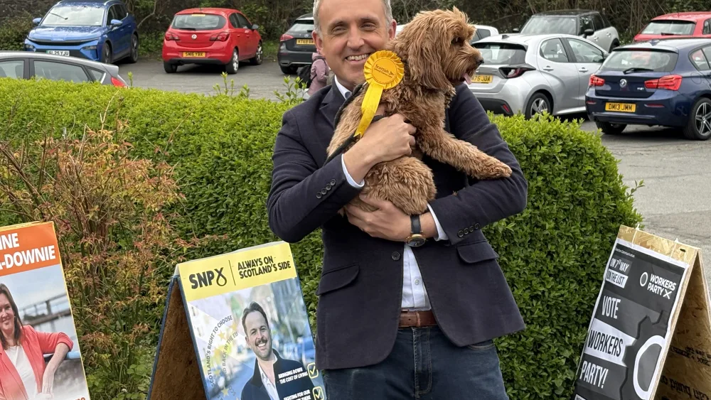 Alex Cole-Hamilton holding his dog and smiling outside a polling place