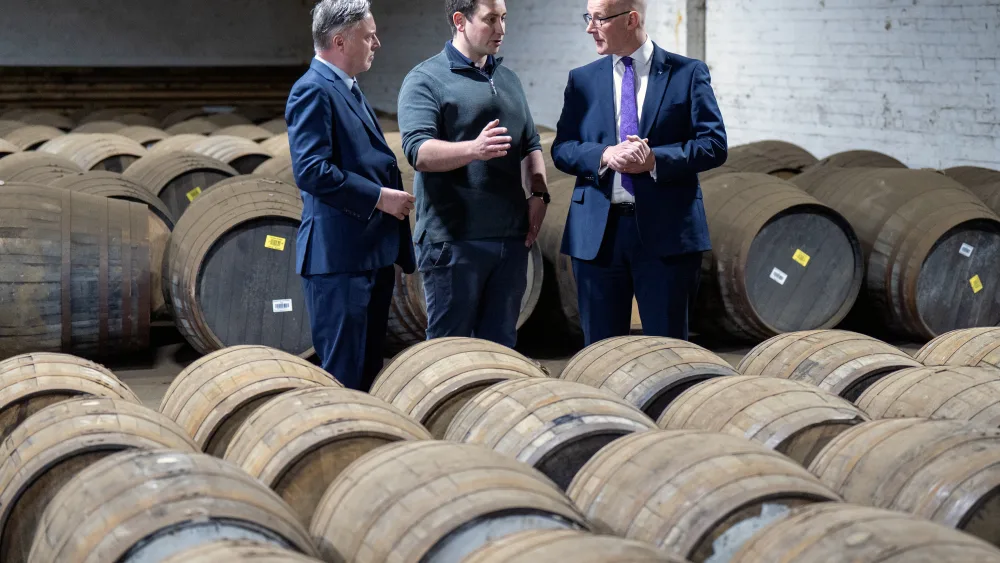 John Swinney standing with two men amongst a large number of whisky casks