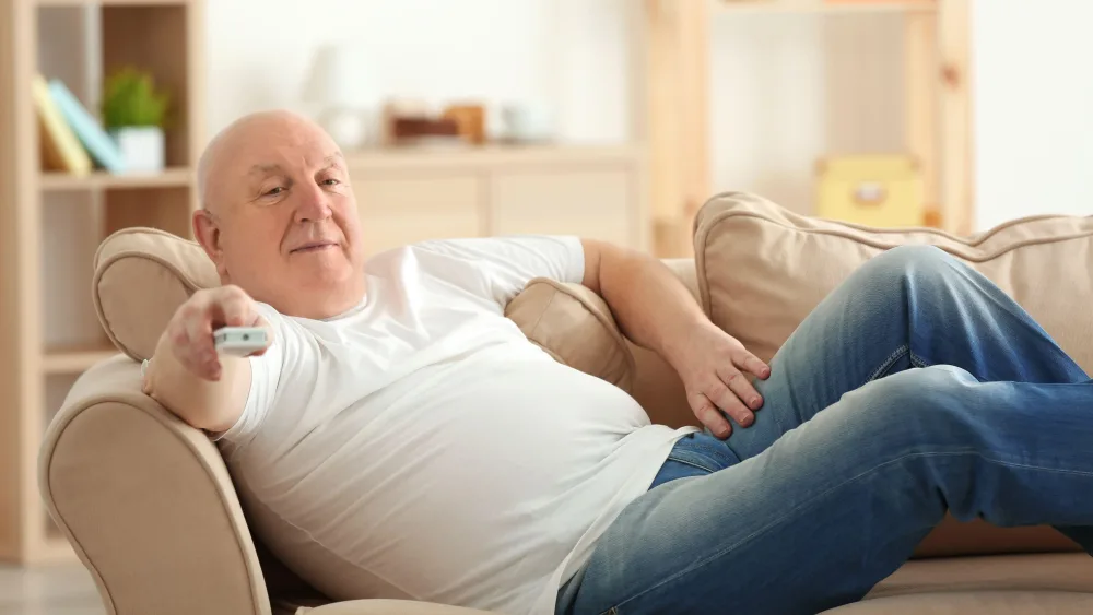 A man lying on a sofa, holding a TV remote