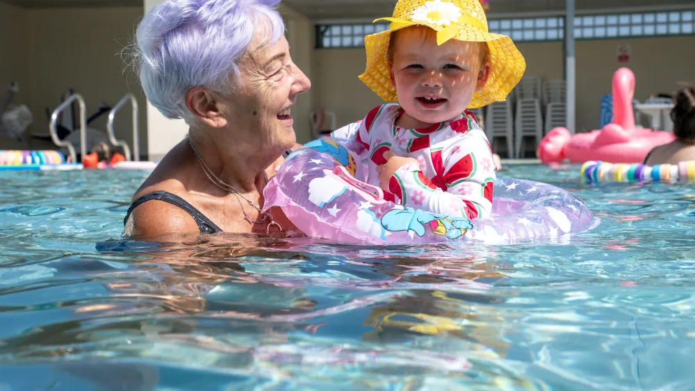 A young girl in a rubber ring with an older lady in an outdoor swimming pool