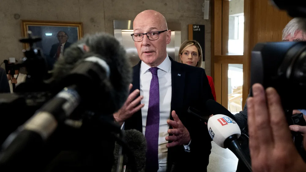 John Swinney speaking in front of a series of microphones and cameras