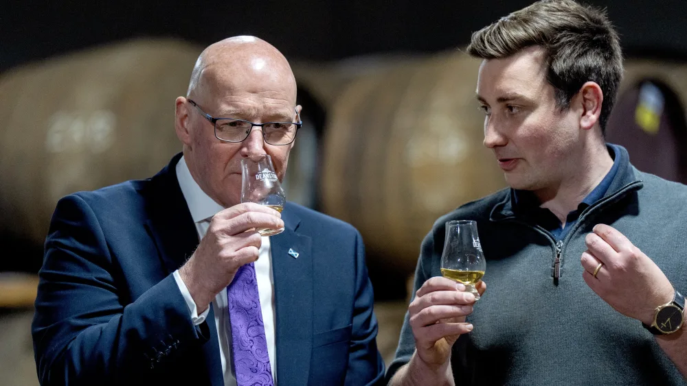 John Swinney holding a glass of whisky, alongside a man who is talking to him