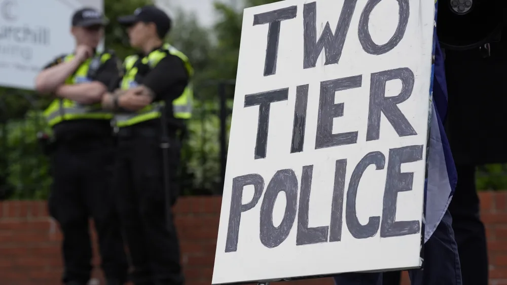 Two police officers in uniform next to a homemade sign reading 'Two tier police'