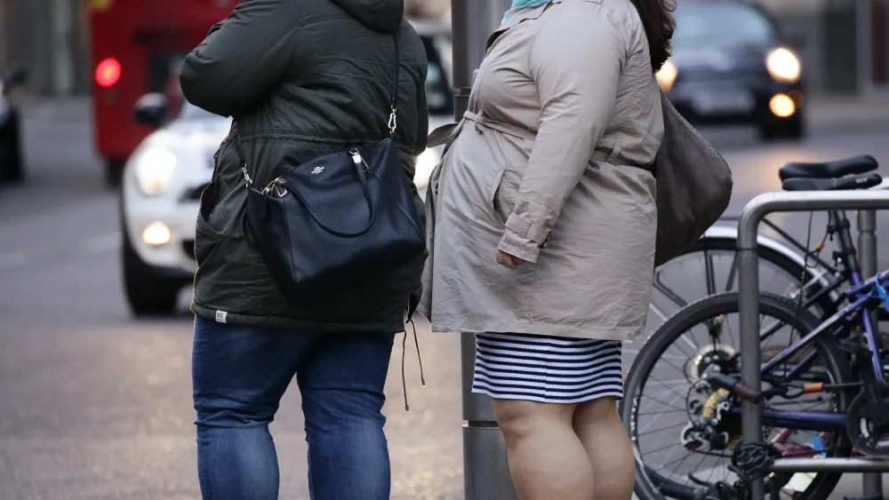 Two women stand and wait to cross a busy road