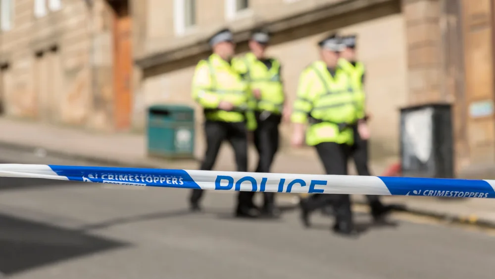 Police tape with four officers walking down a street in the background