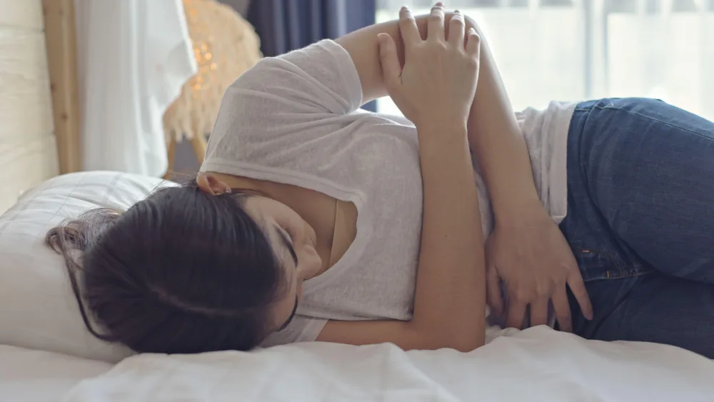 Woman lying on a bed, suffering from stomach pain